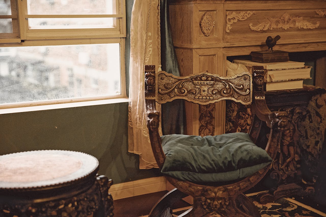 services-04 Luxury vintage interior featuring an ornate wooden chair beside a window with books and decor.